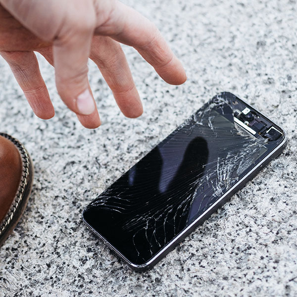 A phone lies on the floor with a cracked screen having been dropped.